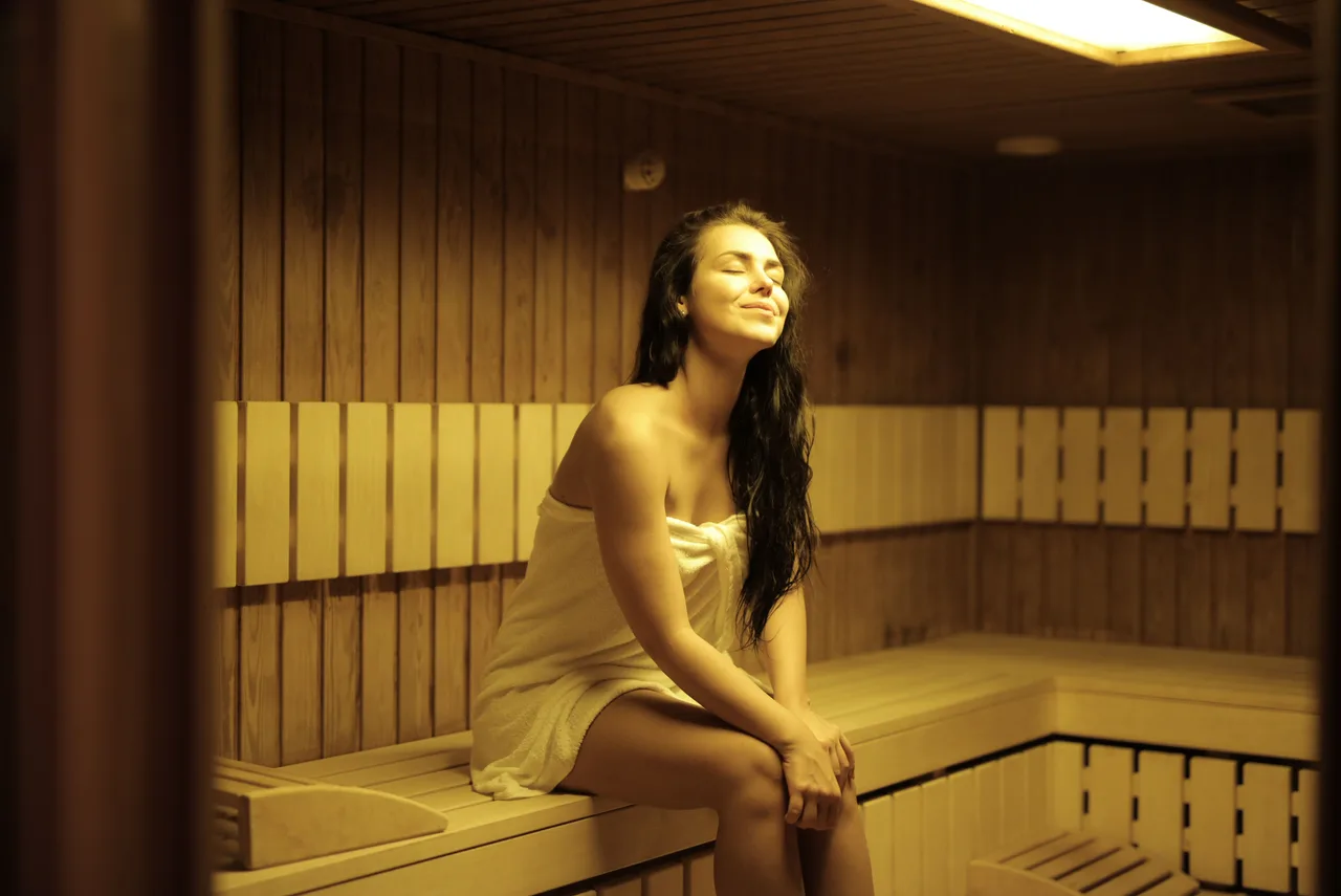 Woman wrapped in a towel relaxing in a wooden sauna.