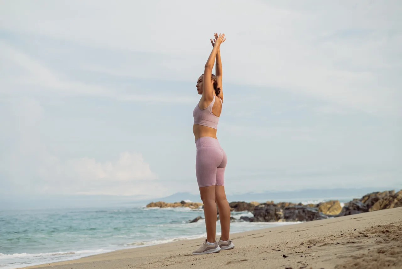 Person stretching with arms overhead on a beach.