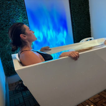 Person seated in a white cold-plunge tub beside a blue illuminated wall.