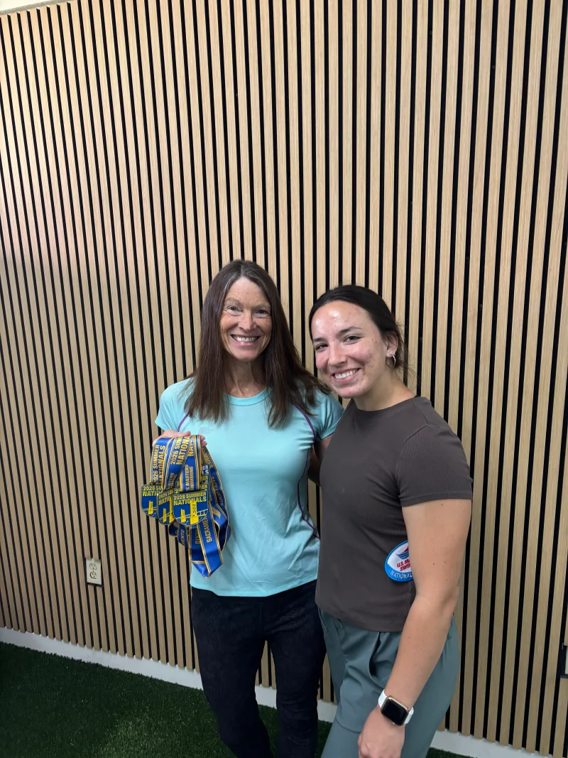 Two people standing together by a wood-slat wall, with one holding several medals.