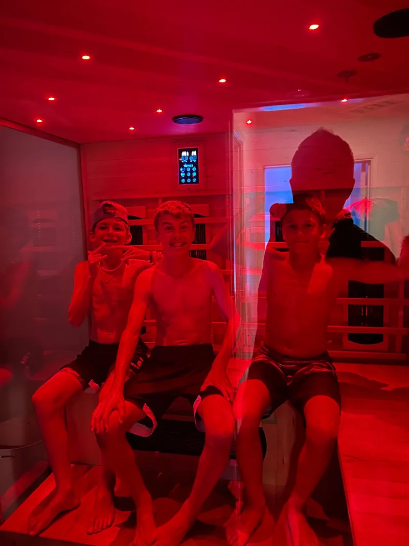 Teammates seated together inside a red-lit sauna.