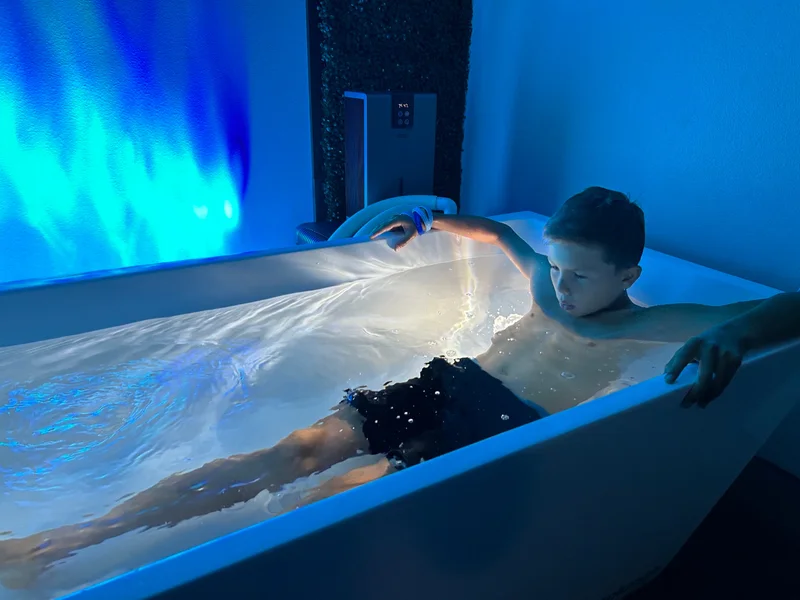 A team participant seated in a cold-plunge tub under blue lighting.