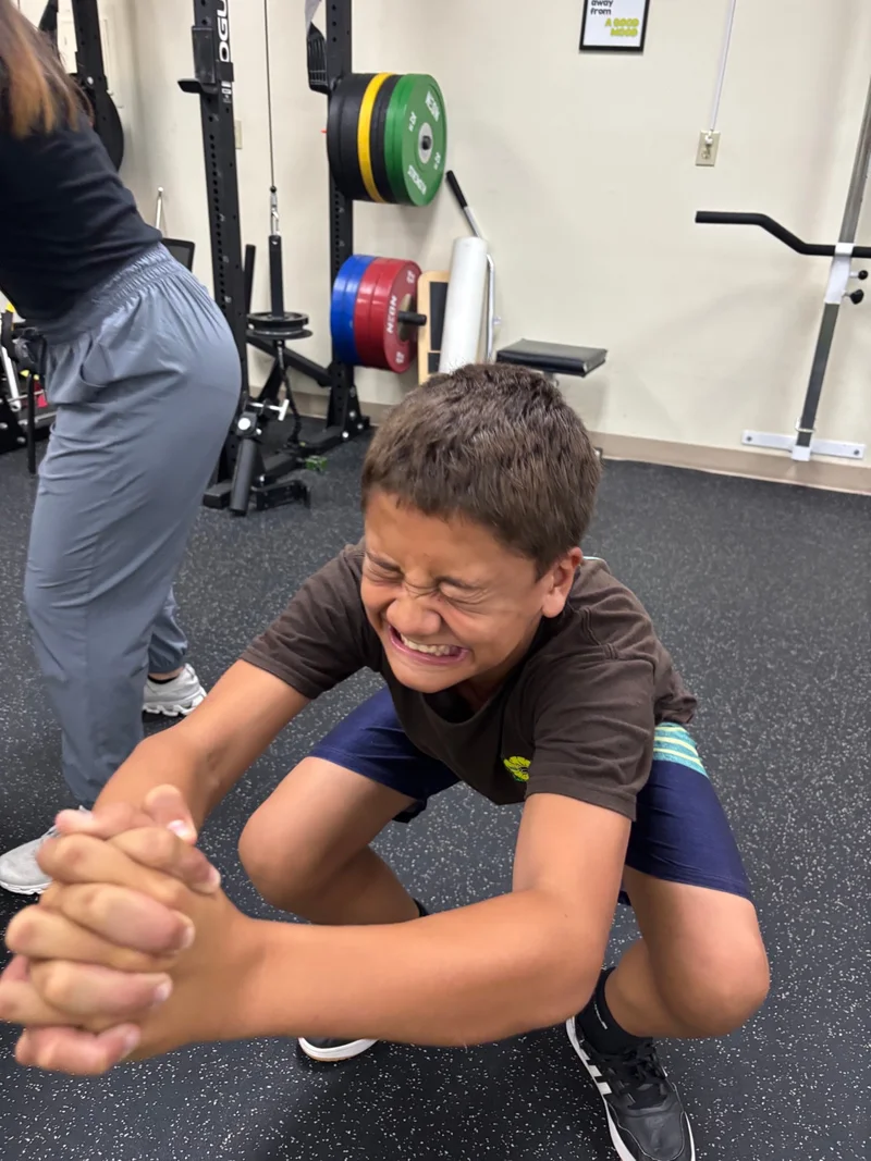 A young athlete practicing a squat in an indoor training space.