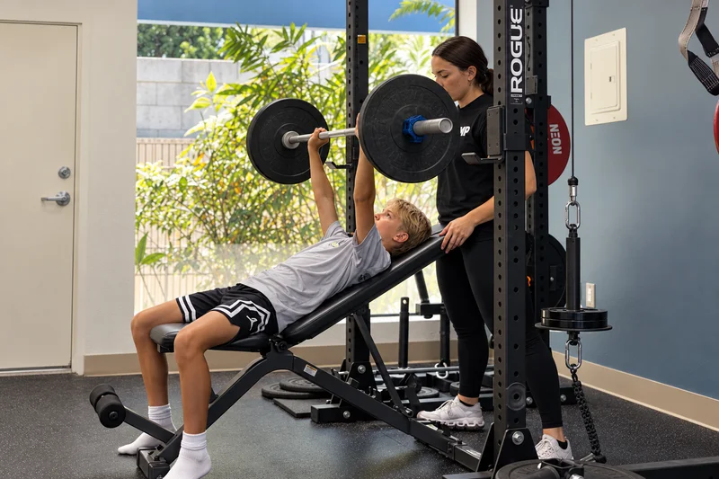 Young athlete performing an incline barbell press with a coach spotting.
